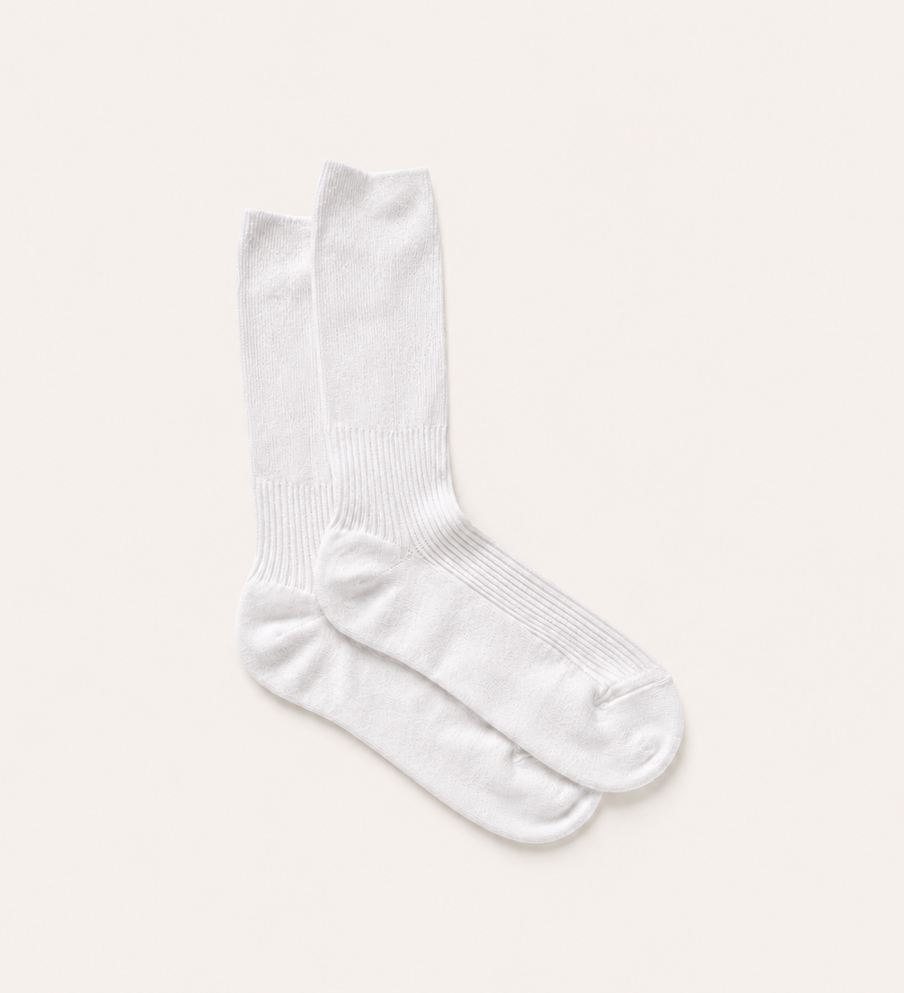 A pair of plain white crew socks laid flat on a light cream background.
